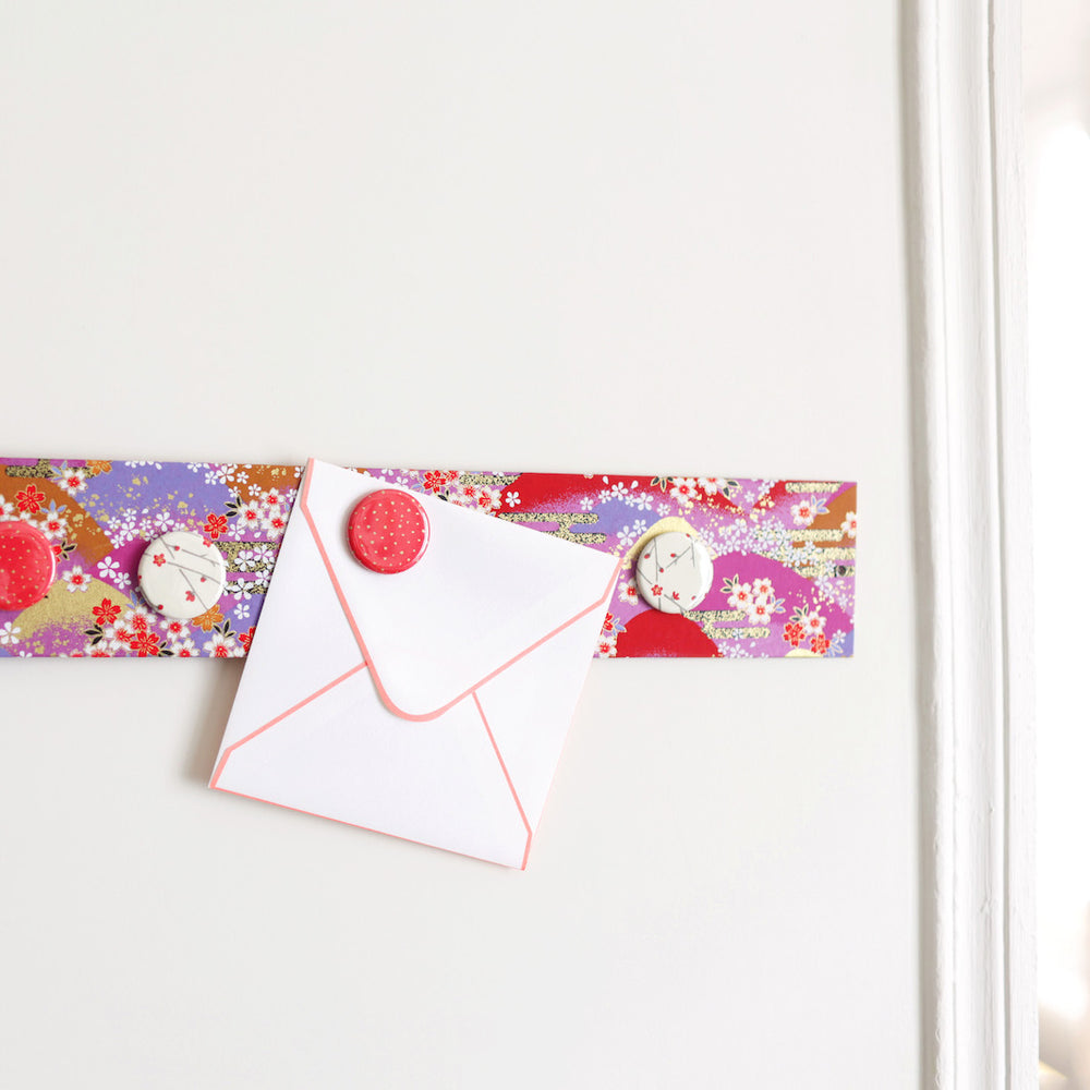photo d'ambiance avec une vue zoomée du pêle-mêle tapissé du papier japonais aux motifs de fleurs, de montagnes et de nuages rouges, roses et violets M948 adeline klam
