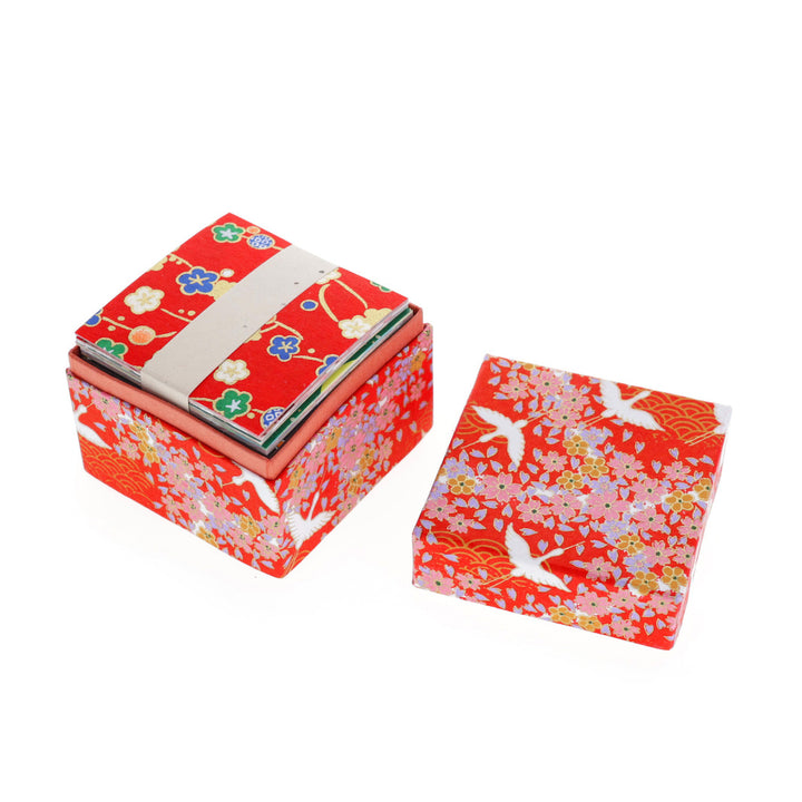 boîte ouverte tapissée d'un papier japonais yuzen adeline klam aux motifs d'envolée de grues et de fleurs sur fond rouge (M322) contenant 200 papiers origami de 6 cm x 6 cm aux motifs variés traditionnels