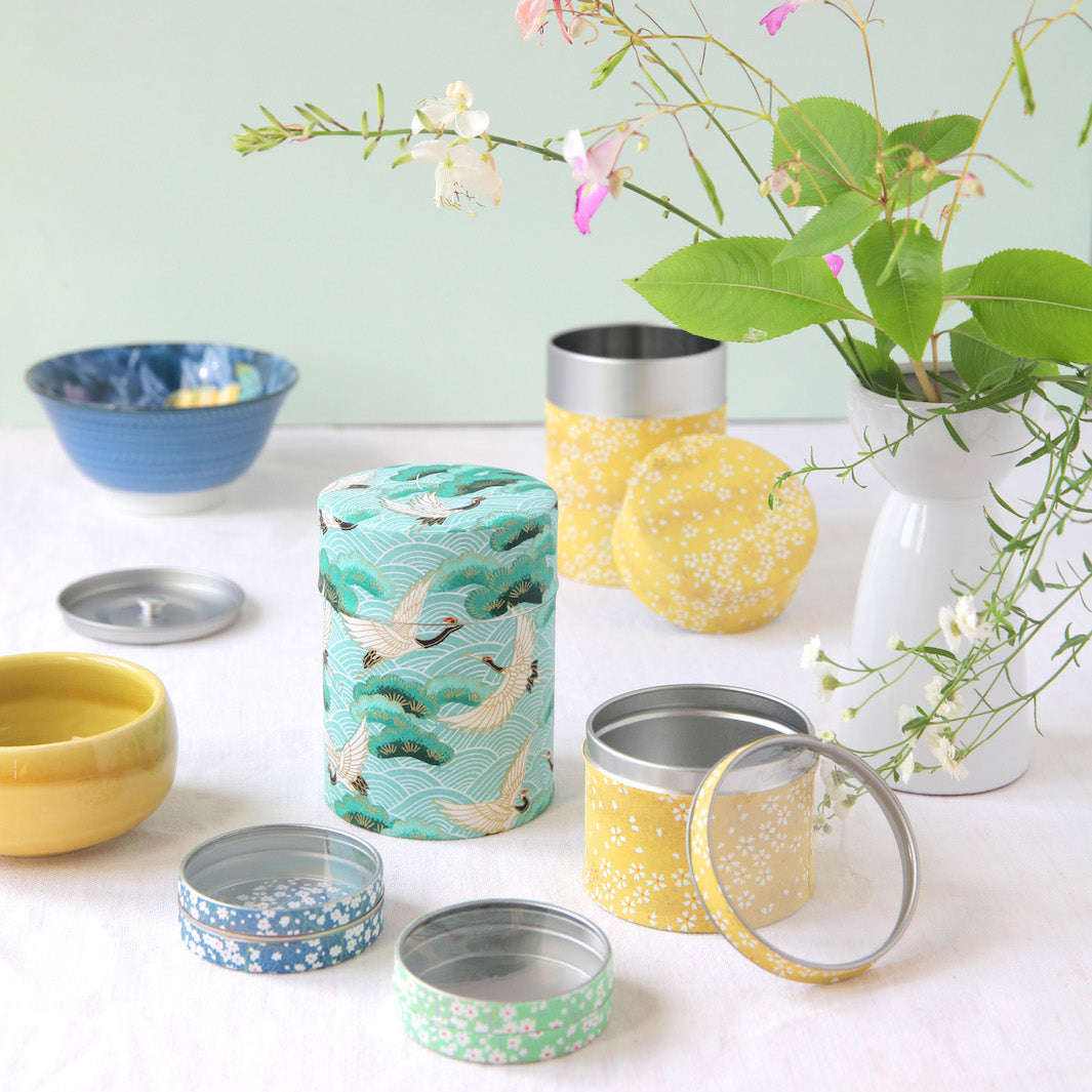 photo d'ambiance de boîtes à thé de forme cylindrique et de taille moyenne dans les tons jaunes, bleus et vert d'eau