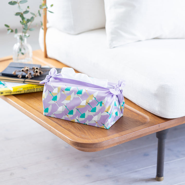 photo d'ambiance d'un emballage de boîte à mouchoirs réalisé avec le furoshiki au motif d'envolée de grues dans les tons violet lilas, jaune moutarde et vert menthe adeline x musubi en 50cm par 50cm
