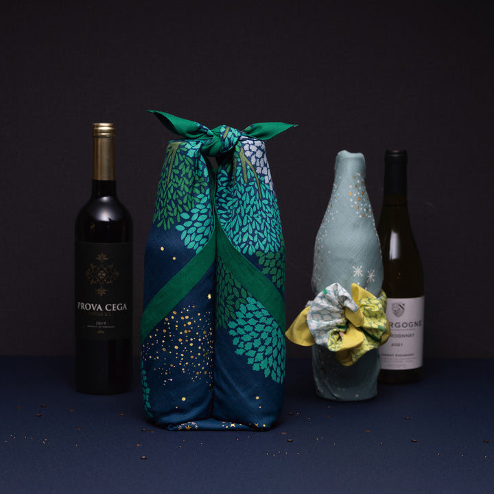 photo d'ambiance de bouteilles de vin emballées avec le furoshiki au motif de forêt étoilée dans les tons bleu marine et turquoise, verts et violet lavande adeline x musubi en 70cm par 70cm