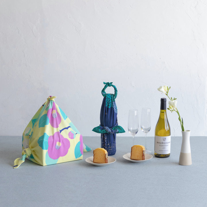 photo d'ambiance de bouteilles de vin emballées avec le furoshiki au motif de forêt étoilée dans les tons bleu marine et turquoise, verts et violet lavande adeline x musubi en 70cm par 70cm