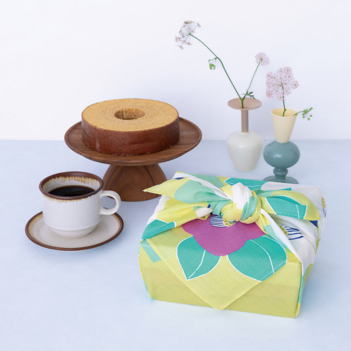 photo d'ambiance d'un emballage cadeau réalisé avec le furoshiki au motif de camélias dans les tons jaune clair, vert d'eau et rose pourpre adeline x musubi en 70cm par 70cm