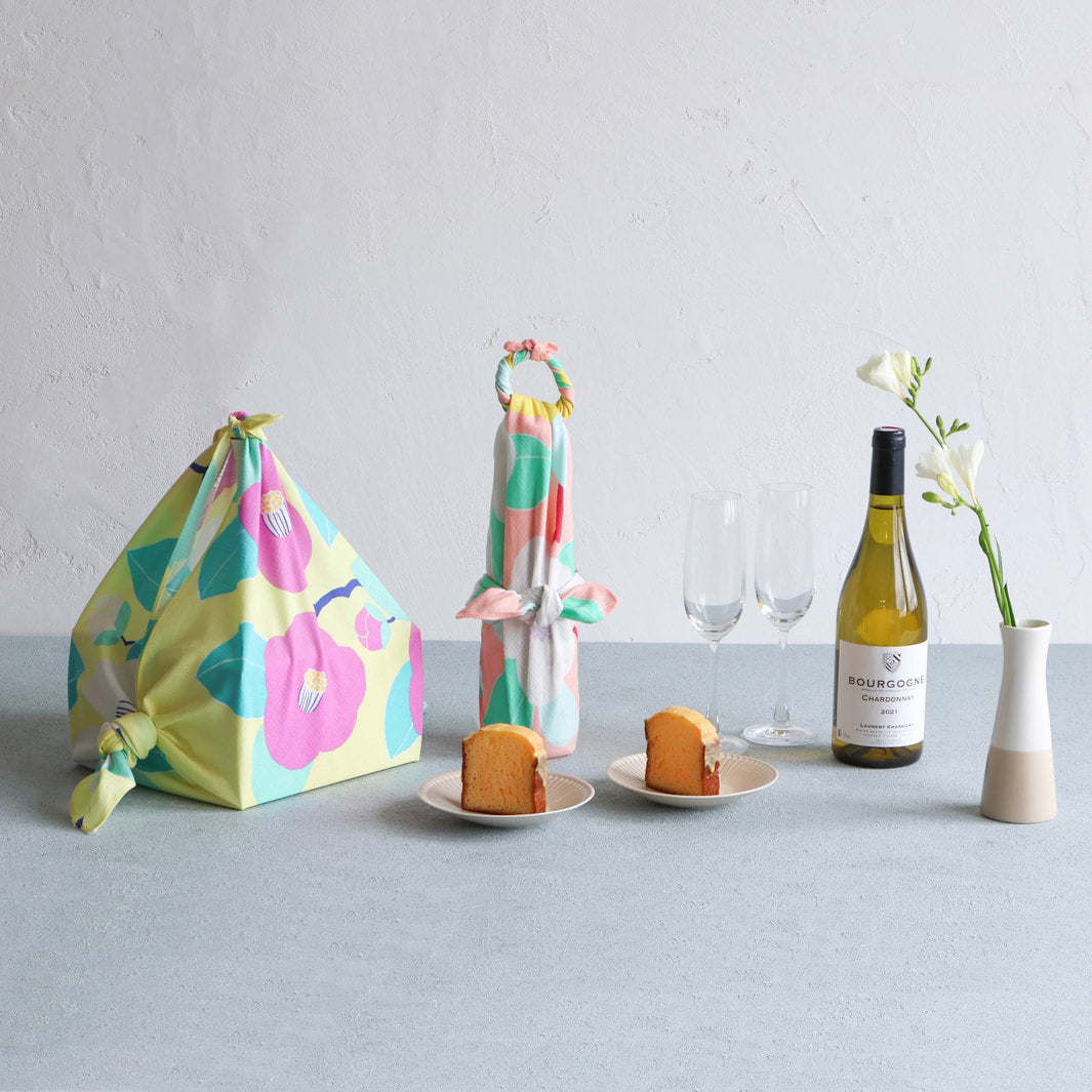 photo d'ambiance d'un emballage cadeau réalisé avec le furoshiki au motif de camélias dans les tons jaune clair, vert d'eau et rose pourpre adeline x musubi en 70cm par 70cm