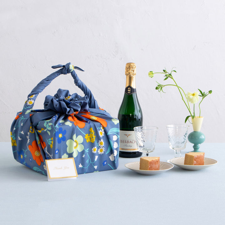 photo d'ambiance d'un emballage cadeau réalisé avec le furoshiki 100x100cm aux motifs garden « orange » dans les tons bleu gris foncé adeline klam x musubi