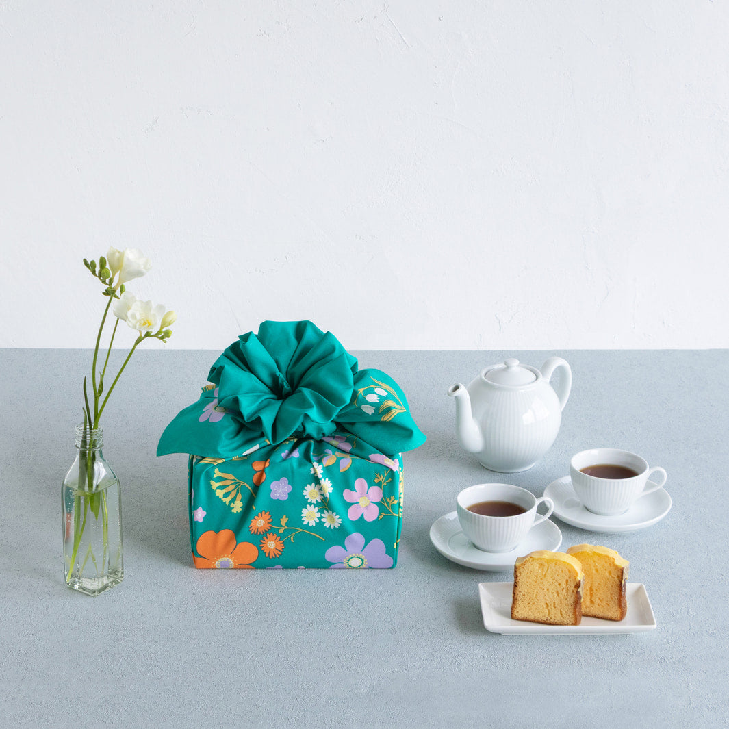 photo d'ambiance d'un emballage cadeau réalisé avec le furoshiki « jardin » dans les tons vert canard, jaunes, violet lilas et orange adeline x musubi en 100cm par 100cm