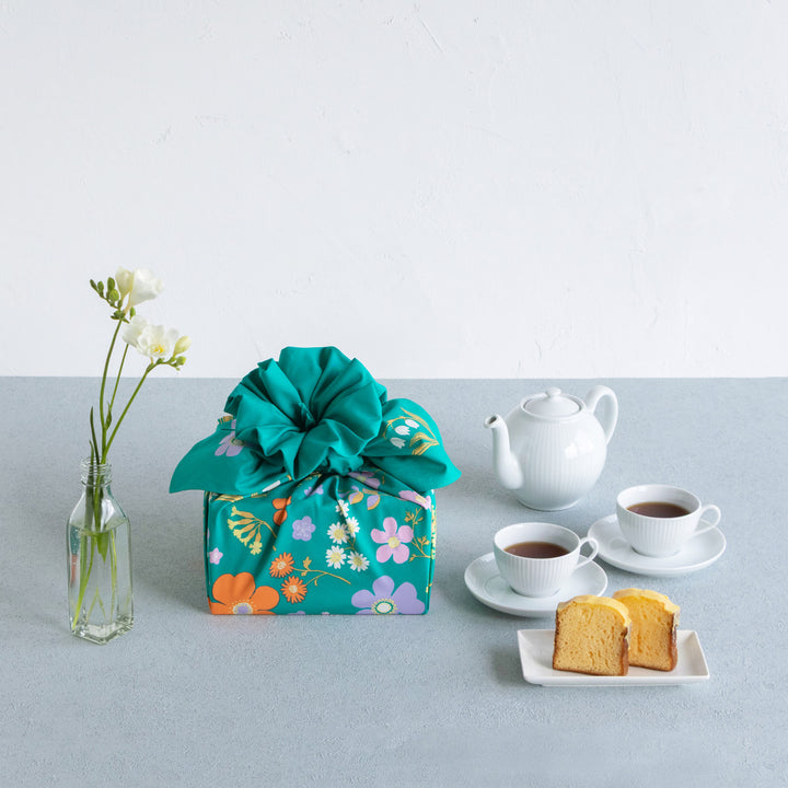 photo d'ambiance d'un emballage cadeau réalisé avec le furoshiki « jardin » dans les tons vert canard, jaunes, violet lilas et orange adeline x musubi en 100cm par 100cm