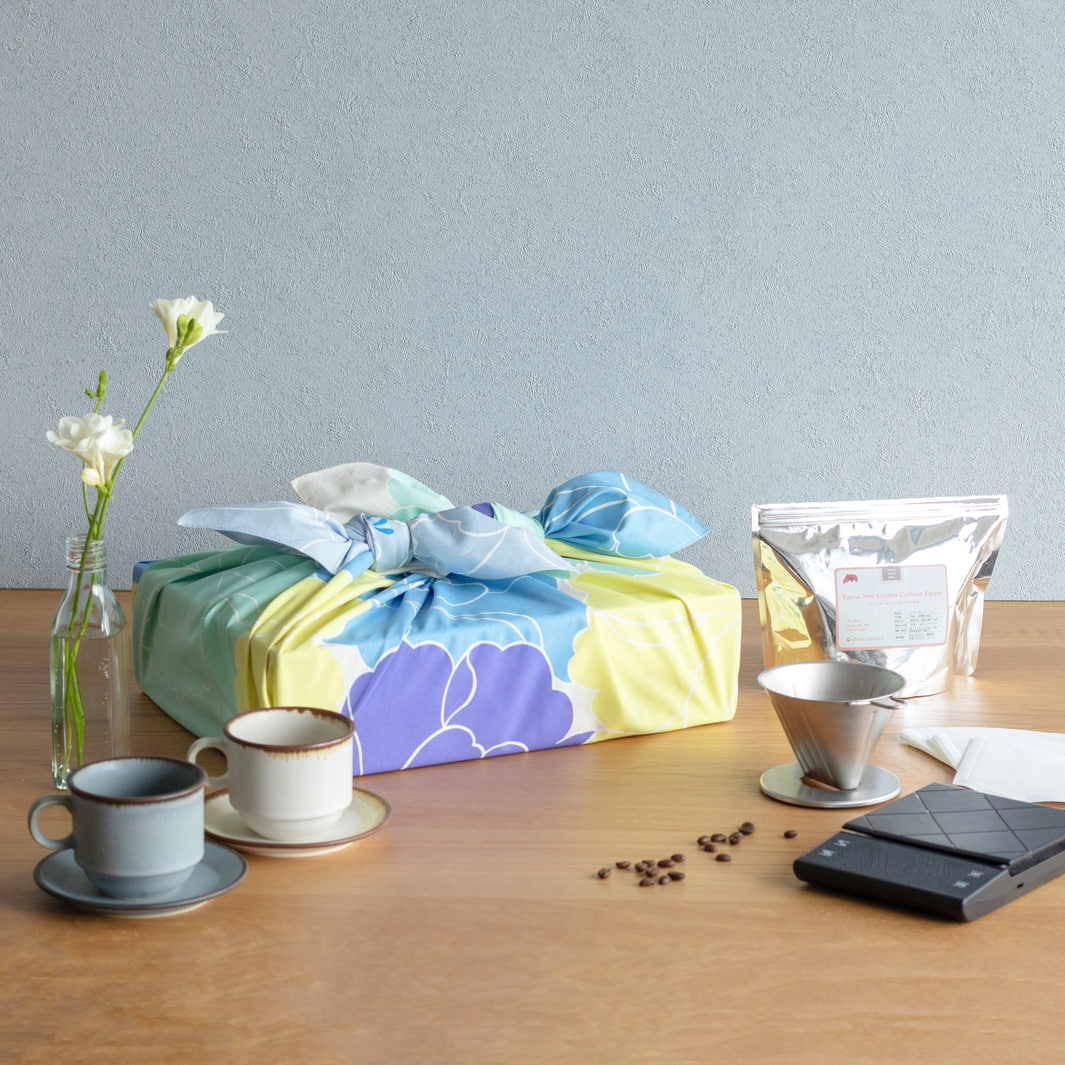 photo d'ambiance d'un emballage cadeau réalisé avec le furoshiki au motif de pivoines dans les tons jaune acidulé, bleus, vert d'eau, violets adeline x musubi en 100cm par 100cm