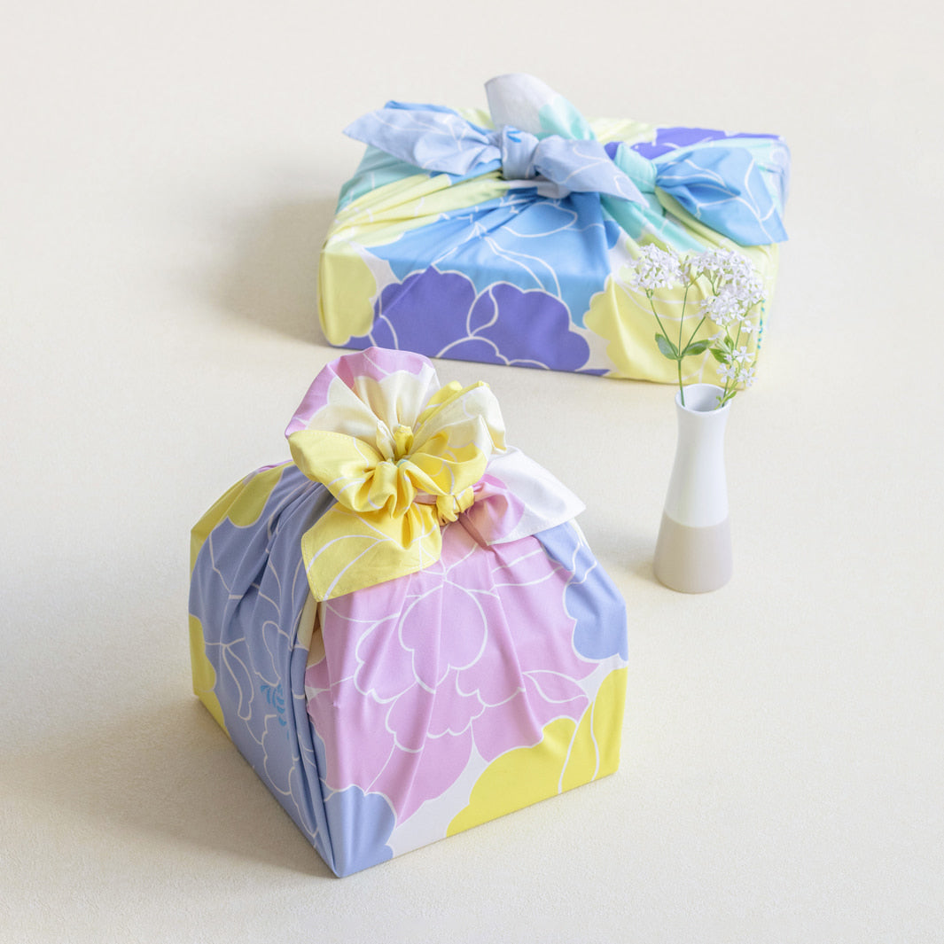photo d'ambiance d'un emballage cadeau réalisé avec le furoshiki au motif de pivoines dans les tons jaune pâle et acidulé, roses et bleu gris adeline x musubi en 100cm par 100cm