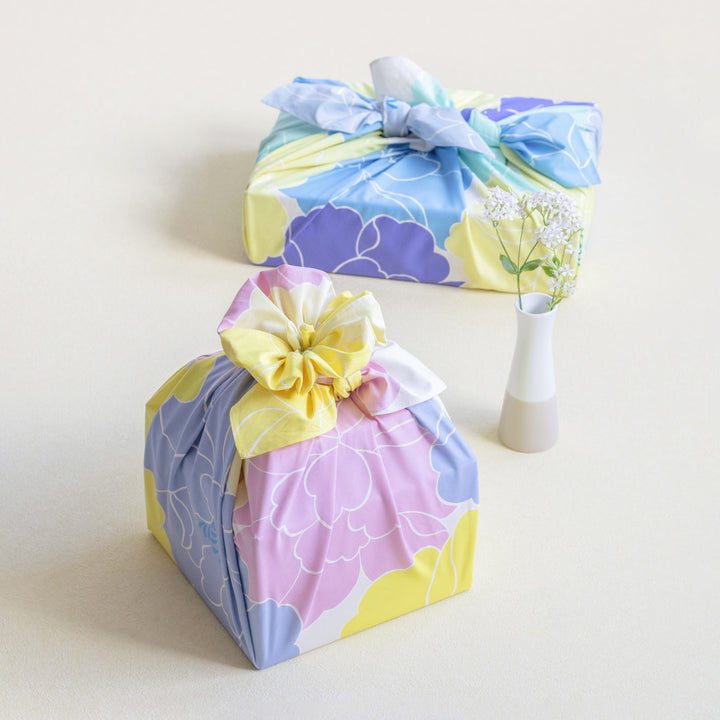 photo d'ambiance d'un emballage cadeau réalisé avec le furoshiki au motif de pivoines dans les tons jaune pâle et acidulé, roses et bleu gris adeline x musubi en 100cm par 100cm