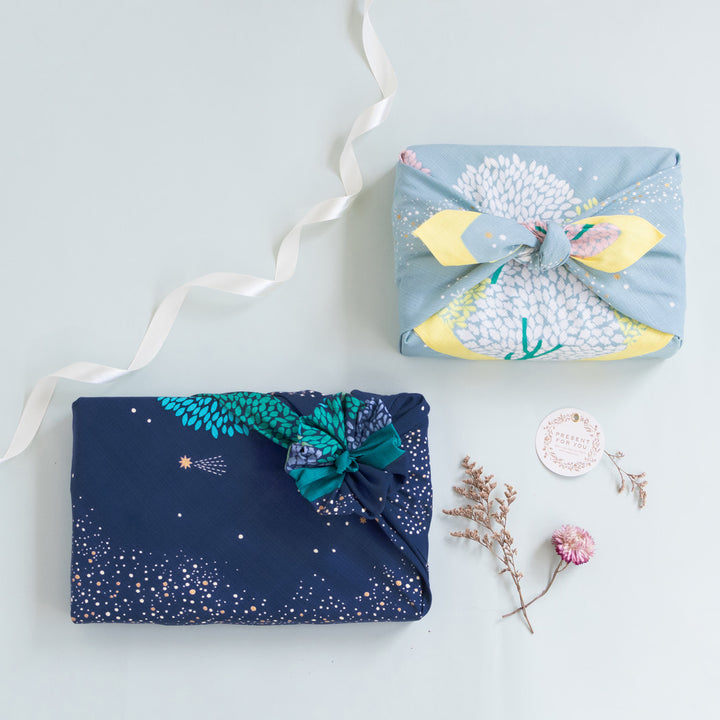 photo d'ambiance d'un emballage cadeau réalisé avec le furoshiki au motif de forêt étoilée dans les tons bleu marine et turquoise, verts et violet lavande adeline x musubi en 70cm par 70cm