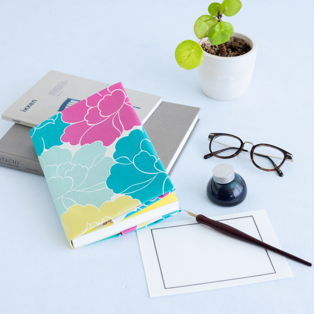 photo d'ambiance d'un emballage de carnet réalisé avec le furoshiki au motif de pivoines dans les tons jaunes, bleu turquoise, rose pourpre et gris vert adeline x musubi en 50cm par 50cm
