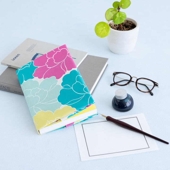 photo d'ambiance d'un emballage de carnet réalisé avec le furoshiki au motif de pivoines dans les tons jaunes, bleu turquoise, rose pourpre et gris vert adeline x musubi en 50cm par 50cm