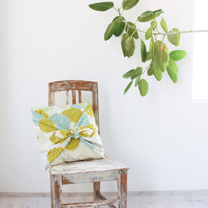 photo d'ambiance d'un emballage de coussin réalisé avec le furoshiki 100x100cm aux motifs de chrysanthèmes « mousse » dans les tons beiges, jaune vert, bleu glacier et vert amande adeline klam x musubi