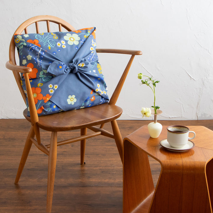 photo d'ambiance d'un emballage de coussin réalisé avec le furoshiki 100x100cm aux motifs garden « orange » dans les tons bleu gris foncé adeline klam x musubi