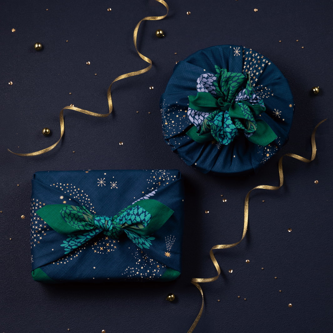 photo d'ambiance d'emballages cadeaux réalisés avec le furoshiki au motif de forêt étoilée dans les tons bleu marine et turquoise, verts et violet lavande adeline x musubi en 70cm par 70cm