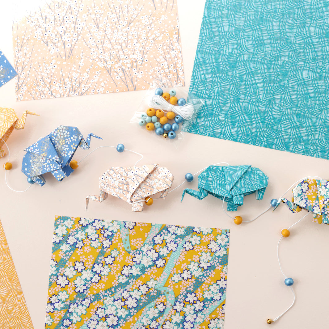 photo d'ambiance de la guirlande montée du kit guirlande d'éléphants en origami dans les tons jaune safran, bleu pervenche, rose clair et bleu canard de la gamme « bombay » adeline klam