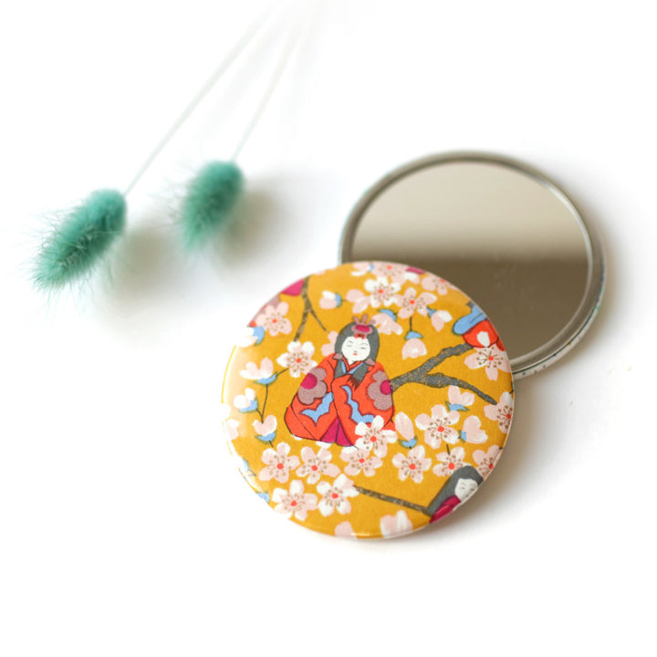 photo d'ambiance du miroir de poche tapissé de papier japonais aux motifs de poupées hina matsuri et fleurs de pêcher dans les tons jaune moutarde, orange vif, rose fuschia, bleu clair et lie de vin (M1006) adeline klam