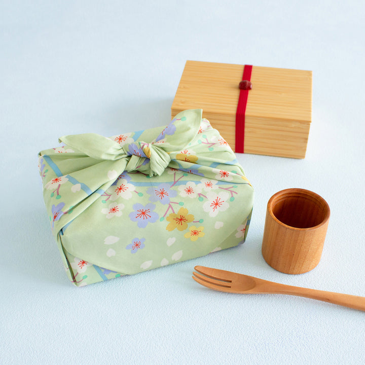 photo d'ambiance d'un emballage de bento réalisé avec le furoshiki 50x50cm aux motifs cerisier « printemps » dans les tons vert amande adeline klam x musubi