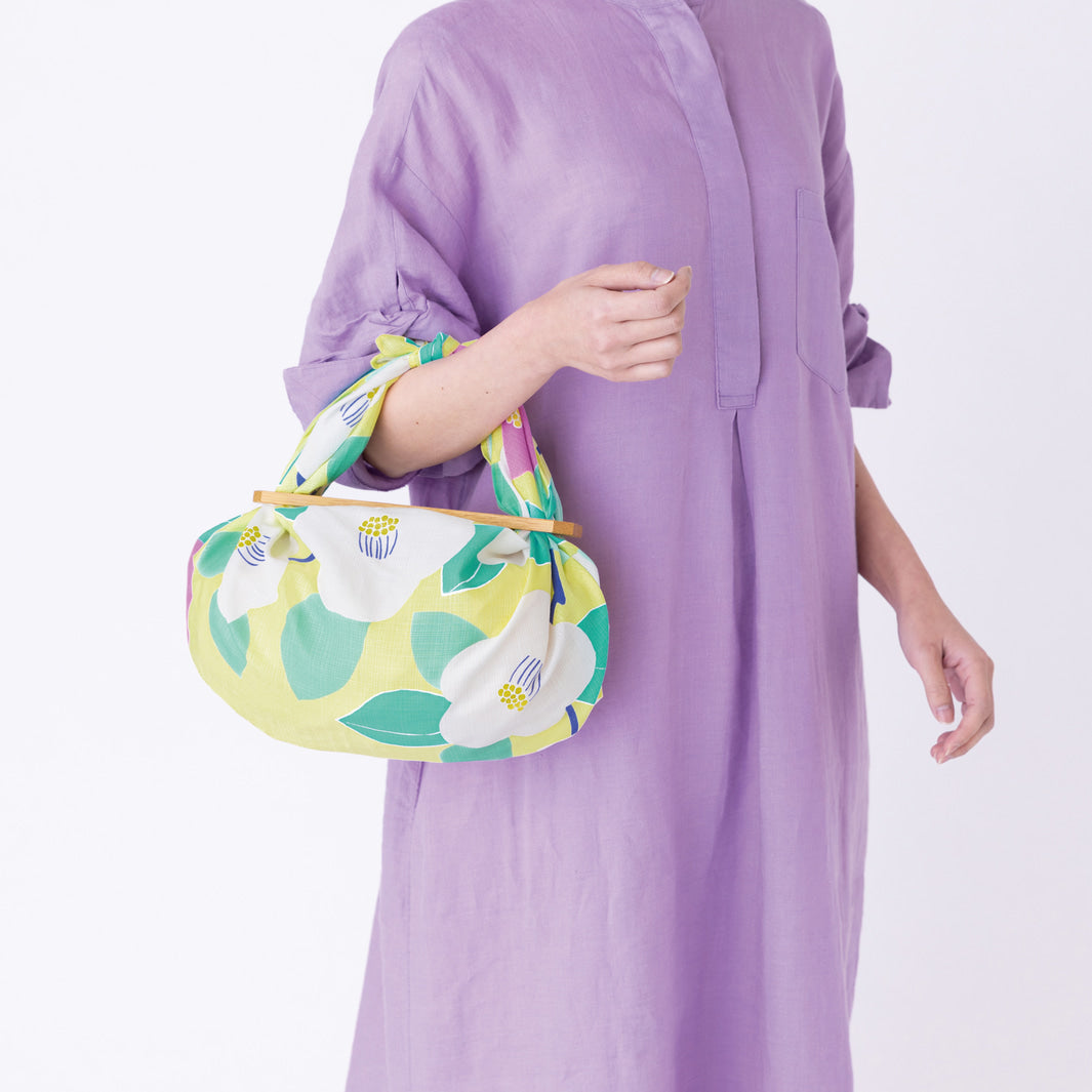 photo d'ambiance d'un sac avec anse réalisé avec le furoshiki au motif de camélias dans les tons jaune clair, vert d'eau et rose pourpre adeline x musubi en 70cm par 70cm