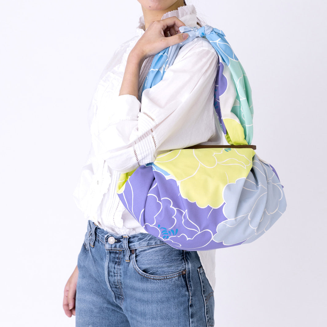 photo d'ambiance d'un sac avec une anse réalisé avec le furoshiki au motif de pivoines dans les tons jaune acidulé, bleus, vert d'eau, violets adeline x musubi en 100cm par 100cm