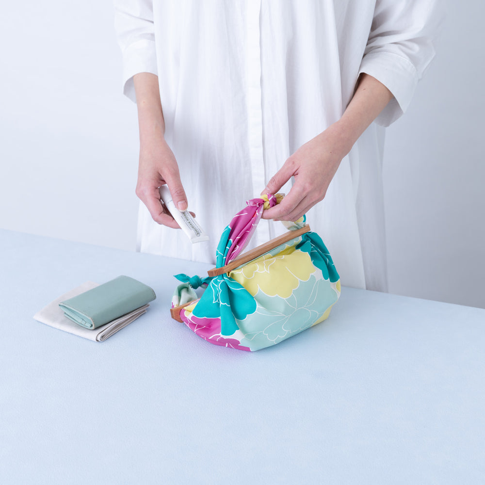 photo d'ambiance d'un emballage de sac réalisé avec le furoshiki au motif de pivoines dans les tons jaunes, bleu turquoise, rose pourpre et gris vert adeline x musubi en 50cm par 50cm