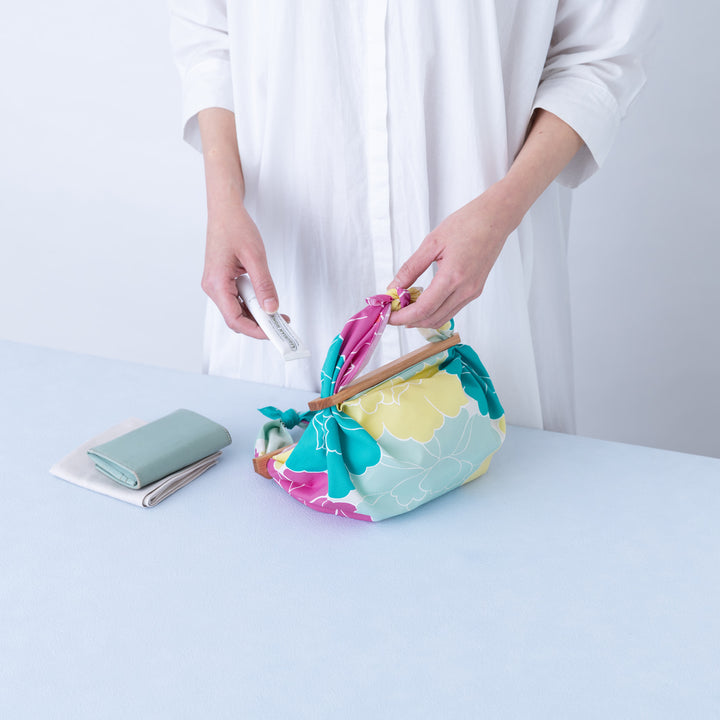 photo d'ambiance d'un emballage de sac réalisé avec le furoshiki au motif de pivoines dans les tons jaunes, bleu turquoise, rose pourpre et gris vert adeline x musubi en 50cm par 50cm