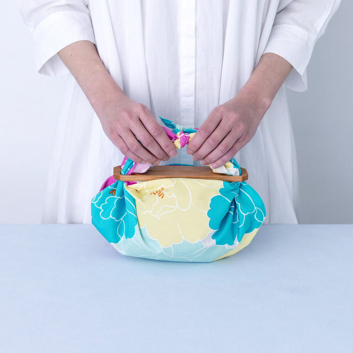 photo d'ambiance d'un emballage de sac réalisé avec le furoshiki au motif de pivoines dans les tons jaunes, bleu turquoise, rose pourpre et gris vert adeline x musubi en 50cm par 50cm
