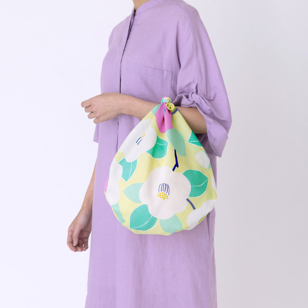 photo d'ambiance d'un sac simple réalisé avec le furoshiki au motif de camélias dans les tons jaune clair, vert d'eau et rose pourpre adeline x musubi en 70cm par 70cm