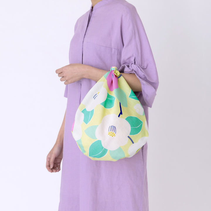photo d'ambiance d'un sac simple réalisé avec le furoshiki au motif de camélias dans les tons jaune clair, vert d'eau et rose pourpre adeline x musubi en 70cm par 70cm