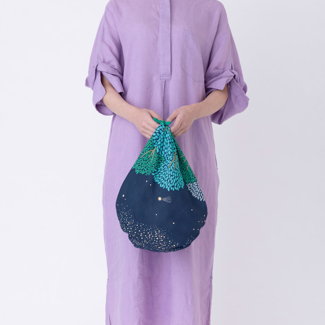 photo d'ambiance d'un sac simple réalisé avec le furoshiki au motif de forêt étoilée dans les tons bleu marine et turquoise, verts et violet lavande adeline x musubi en 70cm par 70cm