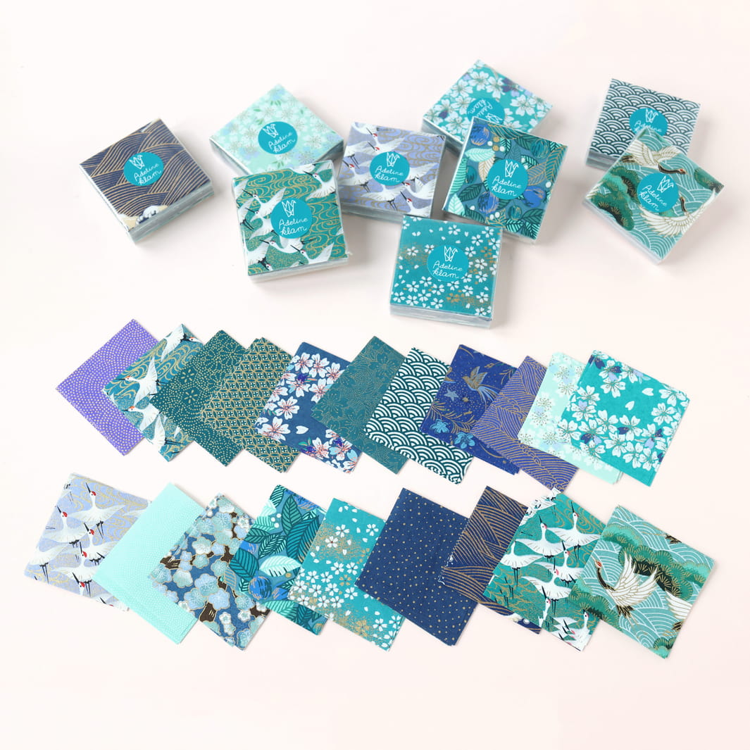 photo d'ambiance de sets de 100 carrés de papiers japonais adeline klam de 6cm par 6cm dans les tons bleu canard, vert d'eau, bleu nuit, turquoise et violets « paon »