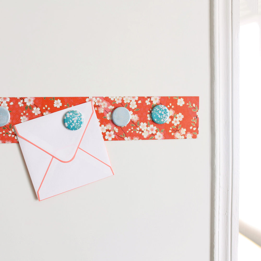 photo d'ambiance avec une vue zoomée du pêle-mêle tapissé du papier japonais aux motifs de fleurs de cerisier et de dessins variés blanc crème, rose clair et rouge orangé M385 adeline klam