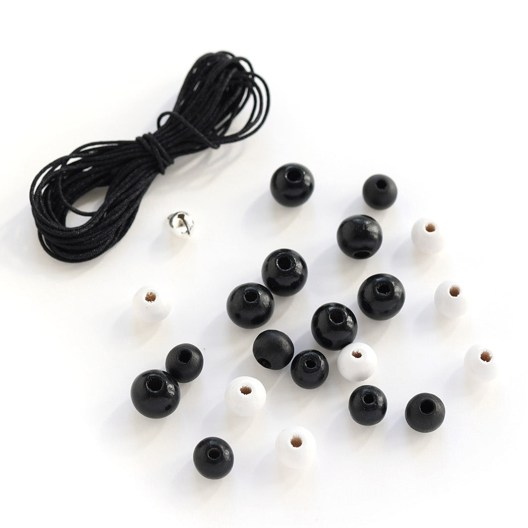 photo packshot d'un lot de 3m de fil noir, de 21 perles noires et blanches et d'un grelot argenté « v » adeline klam