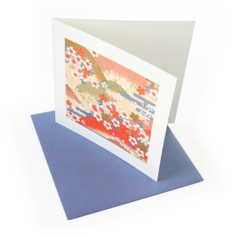 photo packshot vue de biais de la carte carrée double habillée d'un carré de papier japonais de 13cm au motifs de montagnes et de fleurs de cerisier dans les tons jaunes, orange, verts et bleus (M761) et son enveloppe assortie adeline klam