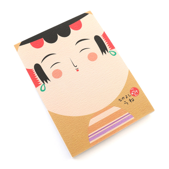 photo packshot de biais de la couverture du bloc-notes de 60 feuilles aux motifs de kokeshi sur fond jaune