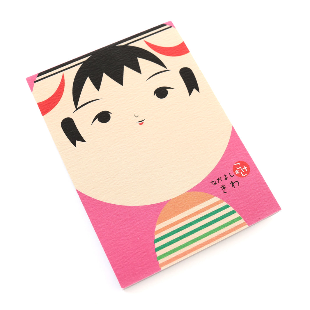 photo packshot de biais de la couverture du bloc-notes de 60 feuilles aux motifs de kokeshi sur fond rose