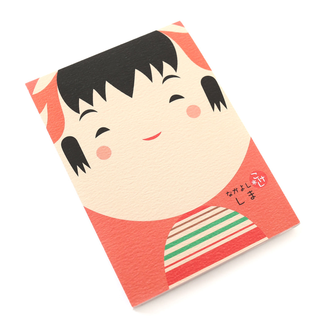 photo packshot de biais de la couverture du bloc-notes de 60 feuilles aux motifs de kokeshi sur fond rouge