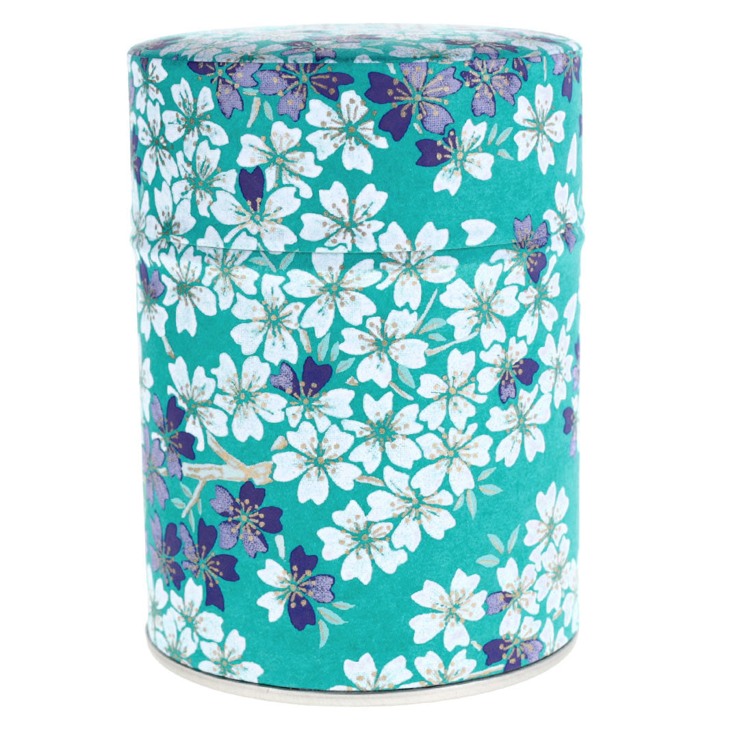 photo packshot d'une boîte à thé cylindrique fermée tapissée de papier japonais aux motifs de fleurs de cerisier dans les tons bleu turquoise, bleu marine, gris violet et blanc (M625) adeline klam