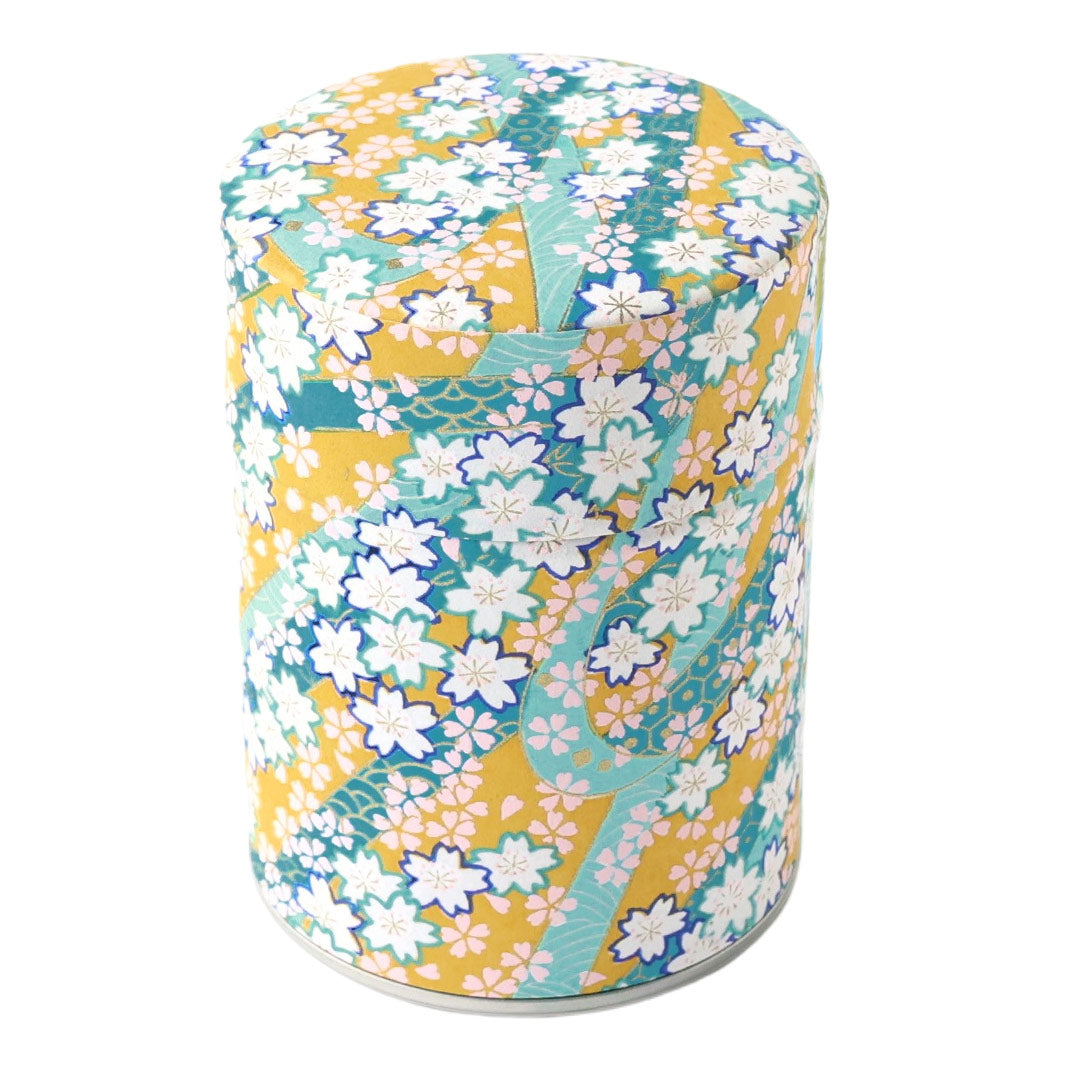 photo packshot d'une boîte à thé cylindrique fermée tapissée d'un papier japonais aux motifs d'ondulations fleuries jaune moutarde, vert d'eau, bleu canard, violet foncé, roses et dorées (M997) adeline klam