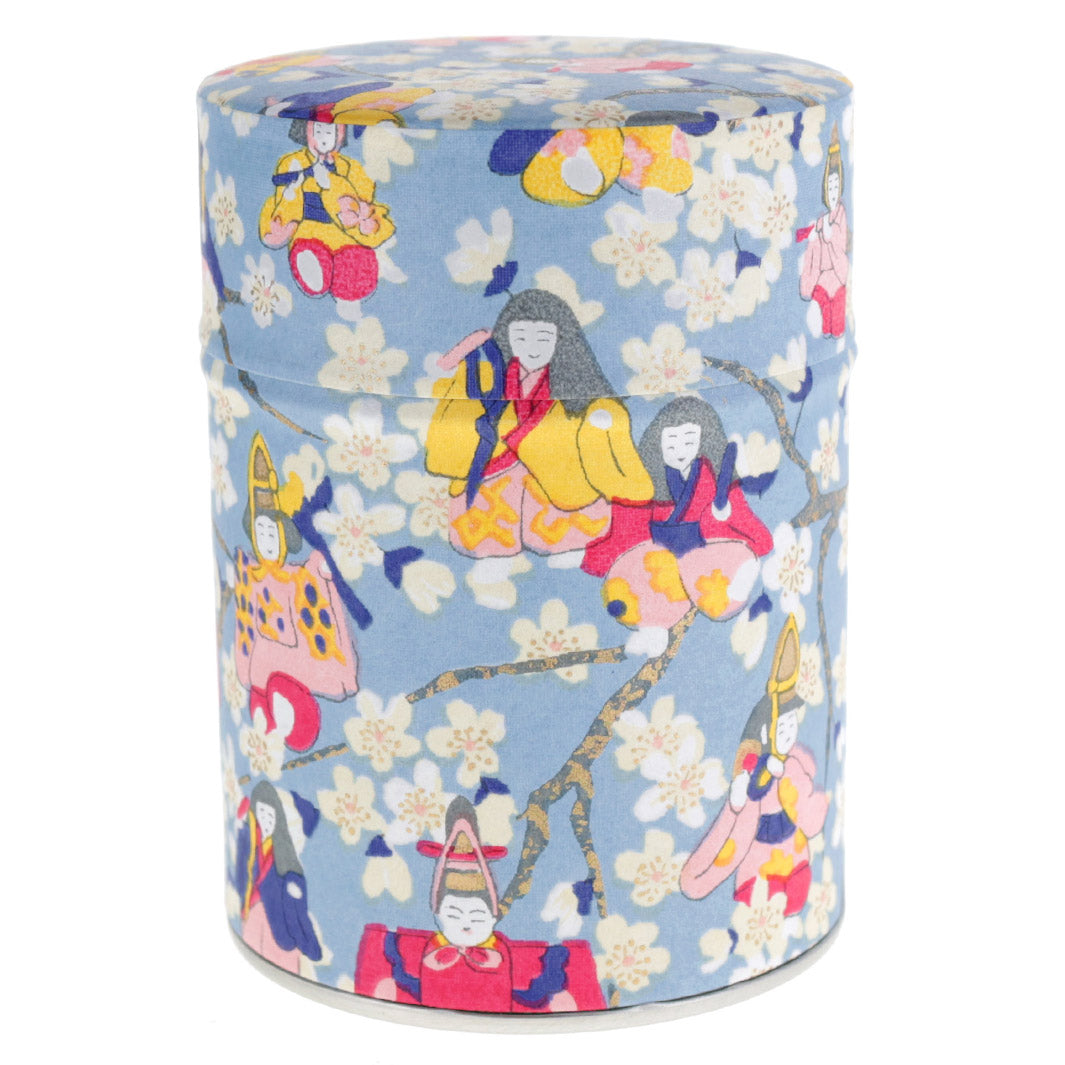 photo packshot d'une boîte à thé cylindrique fermée tapissée de papier japonais aux motifs de poupées d'hina matsuri et de fleurs de pêcher bleu gris, rose rouge, bleu violet, rose clair et jaune (M1005) adeline klam