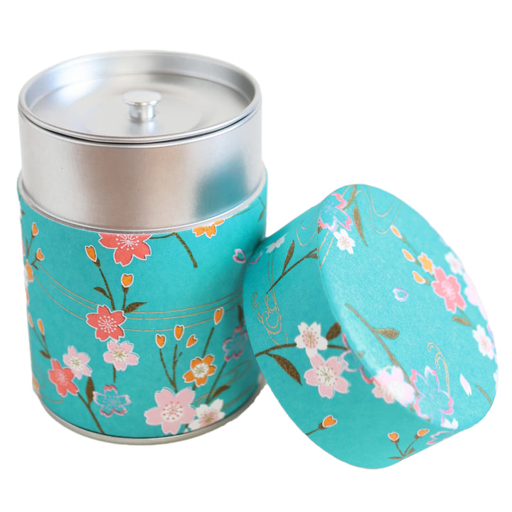 photo packshot d'une boîte à thé cylindrique ouverte tapissée d'un papier japonais aux motifs de branches de fleurs de cerisier et d'ondulations dans les tons bleu turquoise, roses et dorés (M380) adeline klam