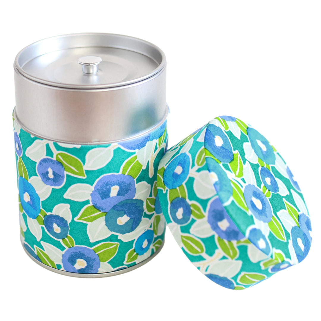 photo packshot d'une boîte à thé cylindrique ouverte tapissée d'un papier japonais aux motifs de camélias dans les tons vert clair, foncé et menthe, bleu moyen et gris (M798) adeline klam