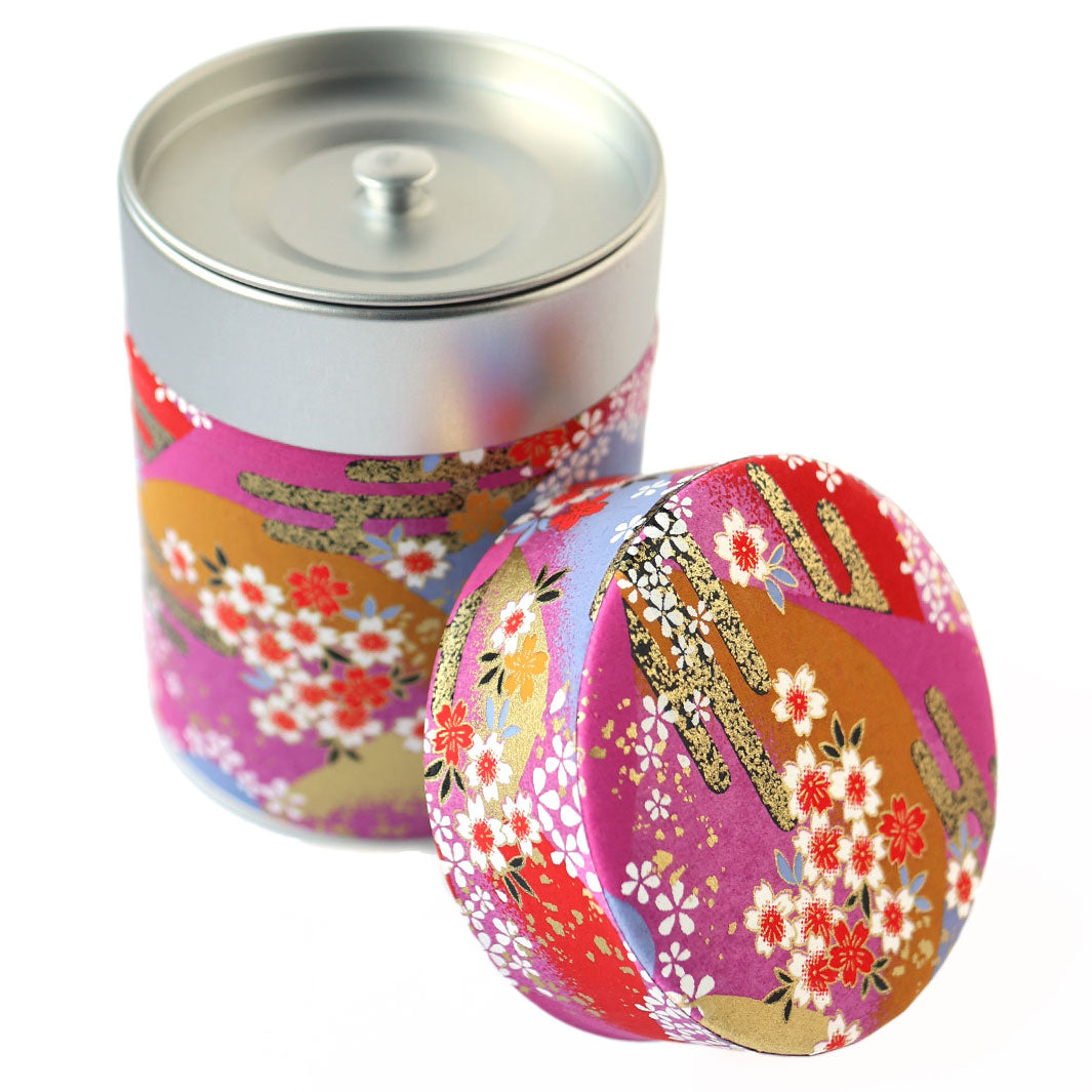 photo packshot d'une boîte à thé cylindrique ouverte tapissée d'un papier japonais aux motifs de de fleurs, de montagnes et de nuages dans les tons rouges, roses, violets et dorés (M948) adeline klam
