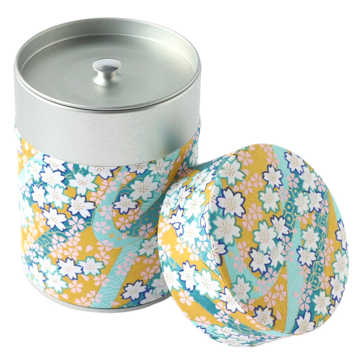 photo packshot d'une boîte à thé cylindrique ouverte tapissée d'un papier japonais aux motifs d'ondulations fleuries jaune moutarde, vert d'eau, bleu canard, violet foncé, roses et dorées (M997) adeline klam