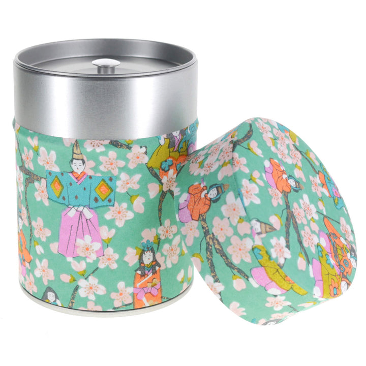 photo packshot d'une boîte à thé cylindrique ouverte tapissée de papier japonais aux motifs de poupées d'hina matsuri et de fleurs de pêcher vert menthe, rose mauve, orange clair, vert acidulé et bleus (M1004) adeline klam