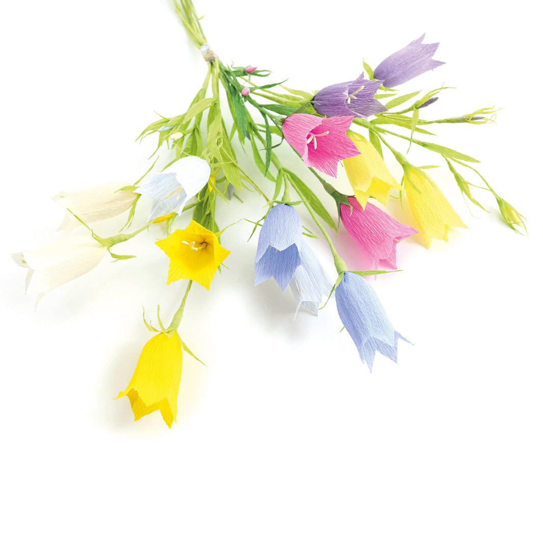 photo packshot des campanules réalisées posées à plat du kit bouquet de campanules en crépon dans les tons bleu violet, bleu ciel, jaunes, ivoire, magenta et vert moyen adeline klam