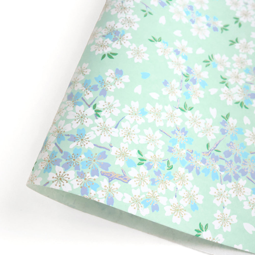 photo packshot d'une courbe de papier japonais yuzen chiyogami au motif de fleurs de cerisier blanches, bleues et mauves sur fond vert d'eau adeline klam (M626)