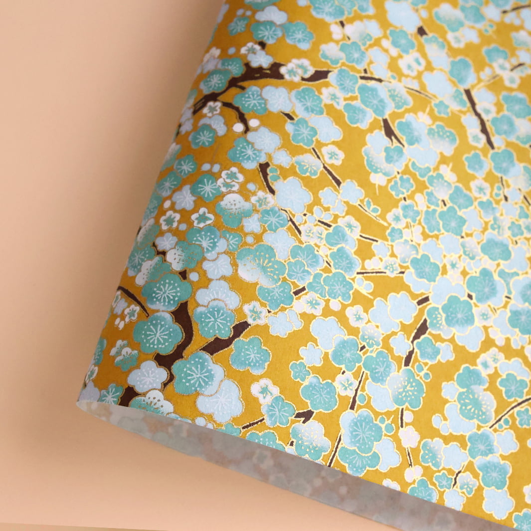 photo packshot d'une courbe de papier japonais yuzen chiyogami aux motifs de fleurs de prunier dans les tons jaune caramel, vert d'eau, bleu ciel et blancs adeline klam (M450)