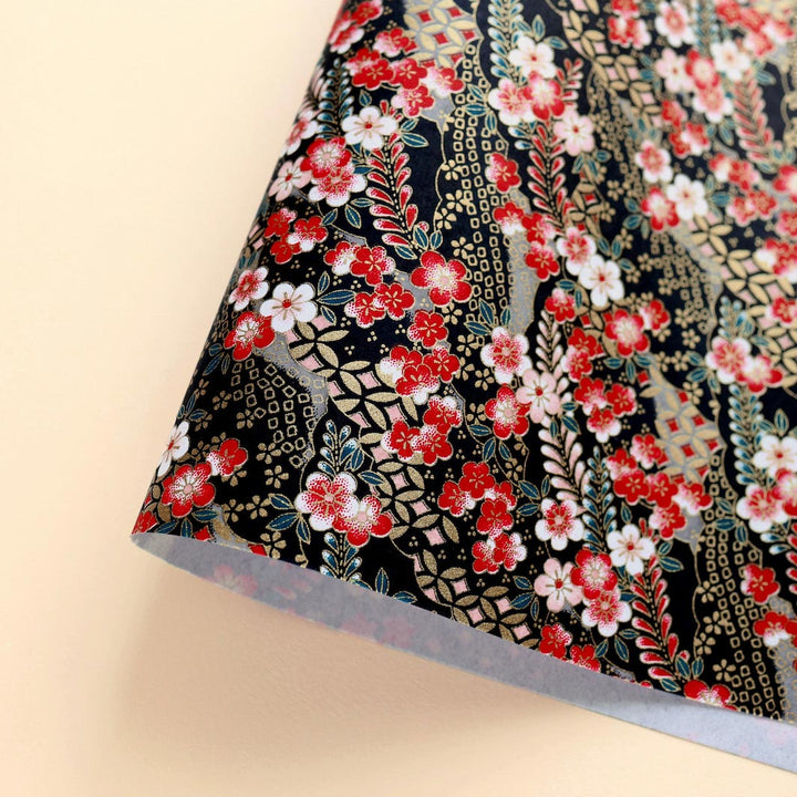 photo packshot d'une courbe de papier japonais yuzen chiyogami aux motifs de fleurs de prunier et de nuages à motifs dans les tons rouges, roses, noirs, bleu canard et dorés adeline klam (M1019)